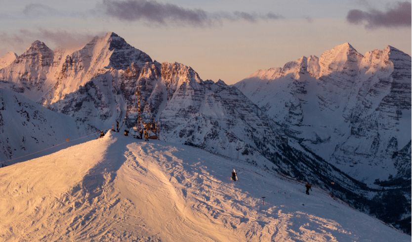 Aspen Highlands bowl at dawn, orange purple light casts on the tall peaks as the prayers fags at the top blow in the wind